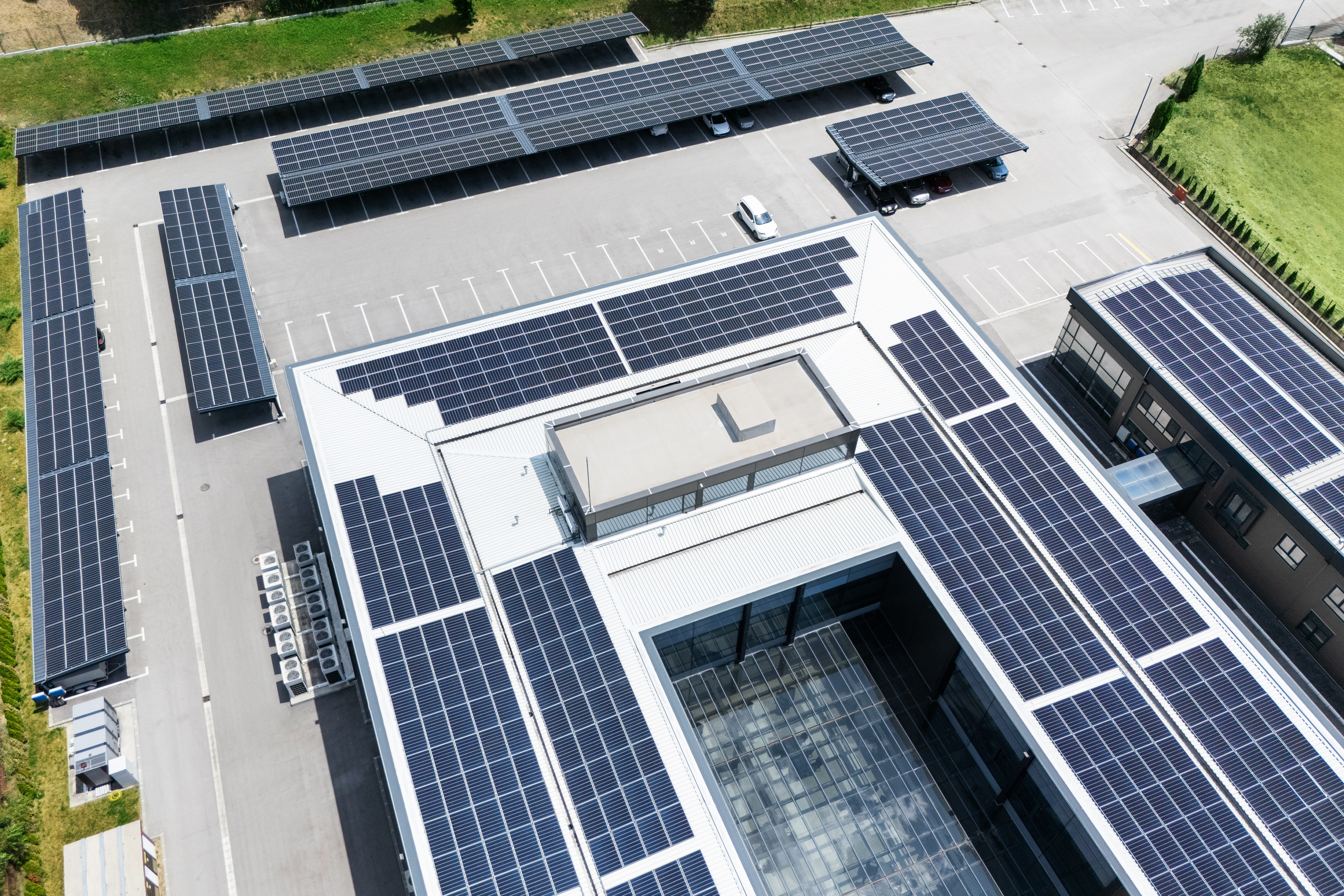aerial view of building with solar panels on a roof and parking space with solar canopies